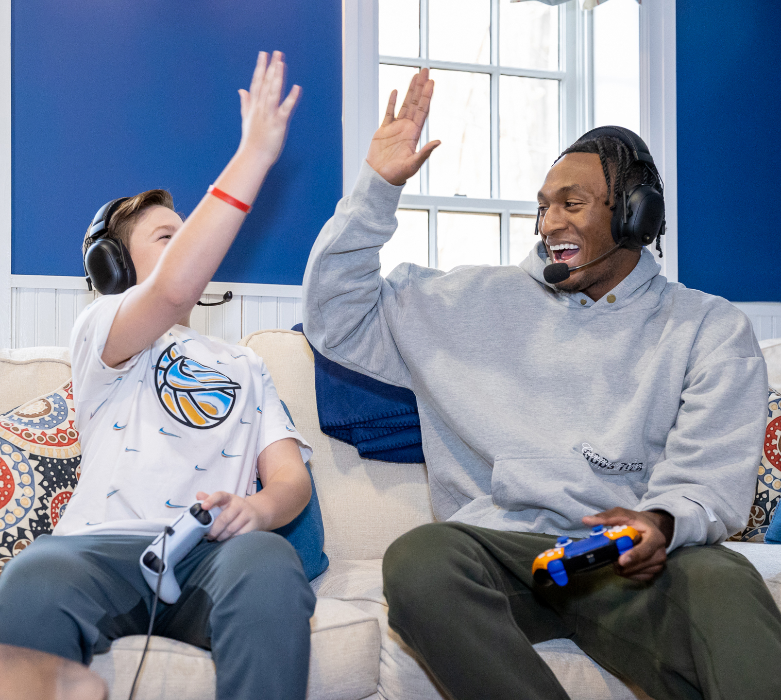 Immanuel Quickley high fives a Garden of Dreams young person while playing video games